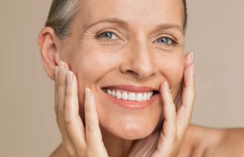 Happy mature woman after anti-aging treatment touching her face with hands