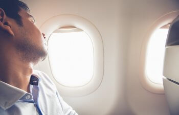 A man in a plane window seat sleeping during his flight