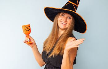 Happy brunette woman in halloween witch black hat holding glass of cocktail.